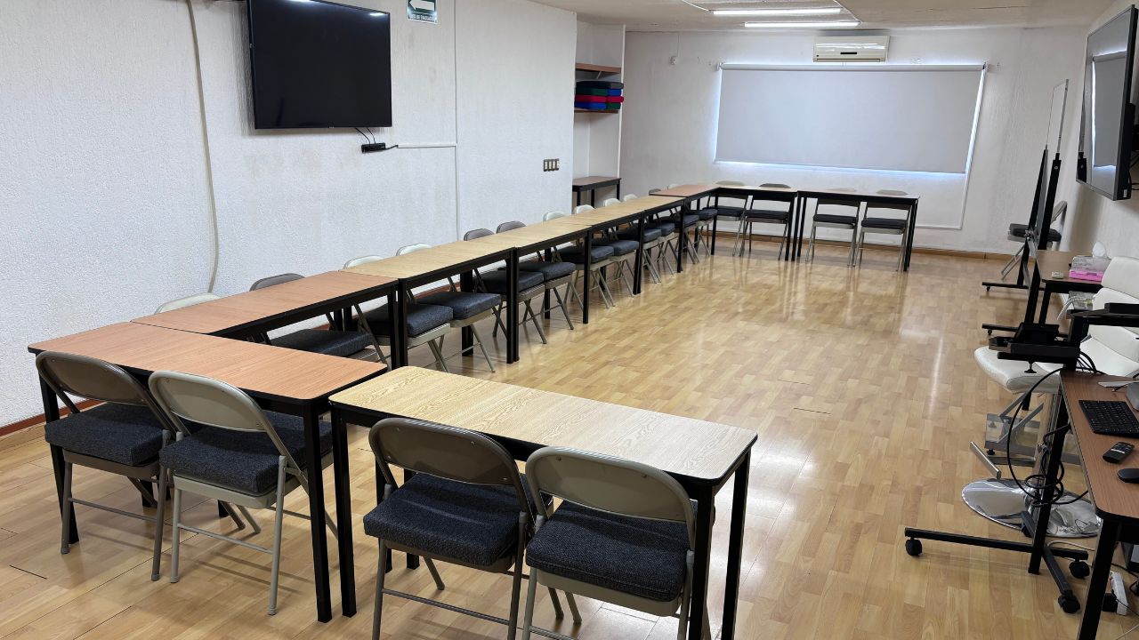 Aula con mesas acomodadas en herradura y pantallas en ambos extremos