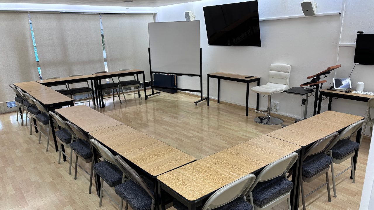 Aula amplia con mesas en herradura, pizarrón blanco y pantalla